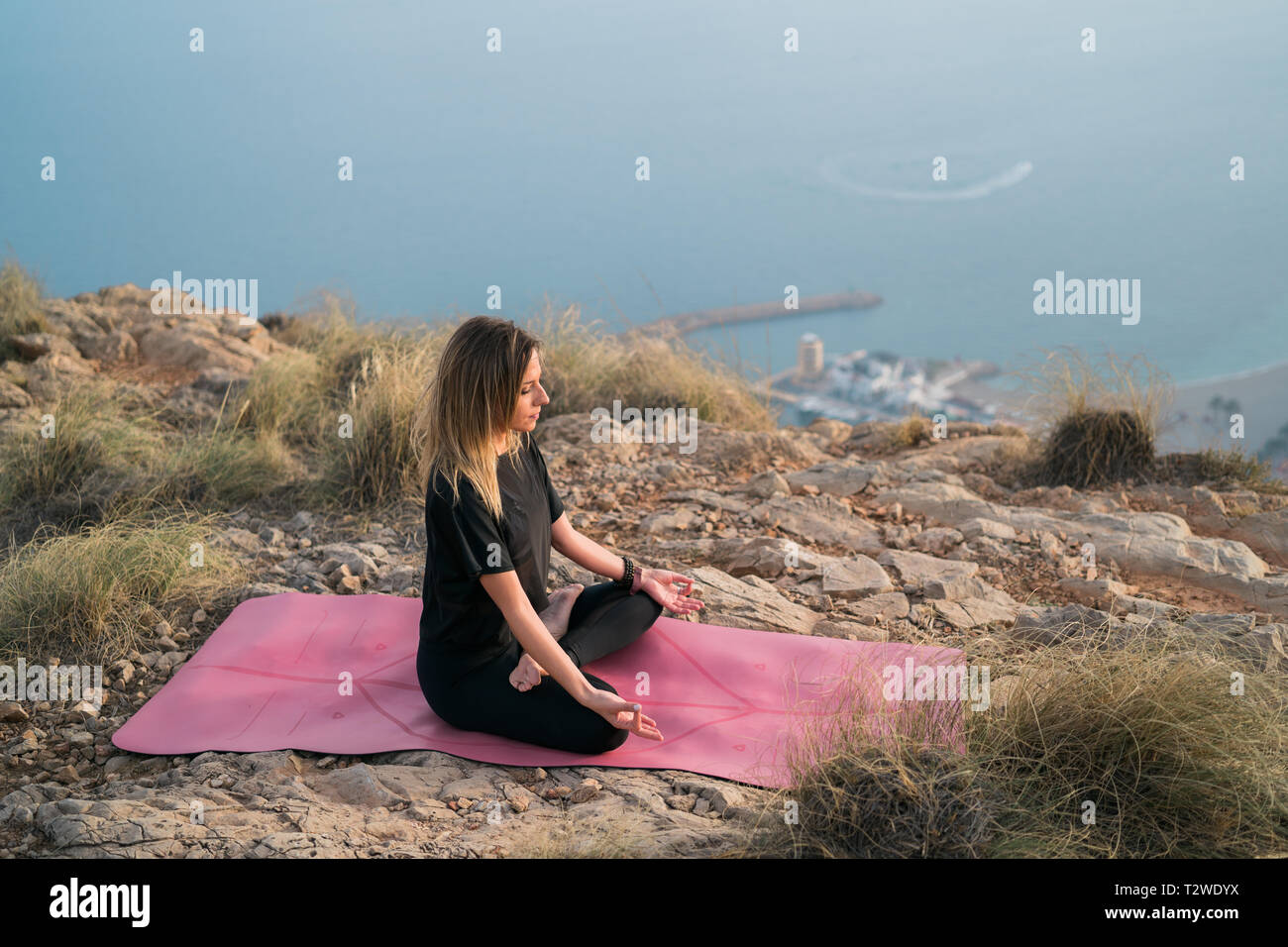Beautiful young woman doing yoga at the top of the mountain with views ...