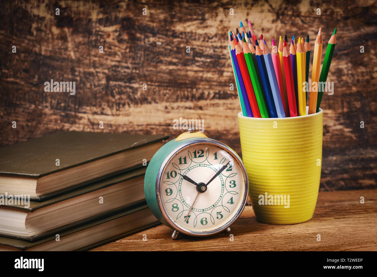 https://c8.alamy.com/comp/T2WEEP/colored-pencils-in-a-glass-next-to-books-and-watche-education-concept-on-a-wooden-background-T2WEEP.jpg