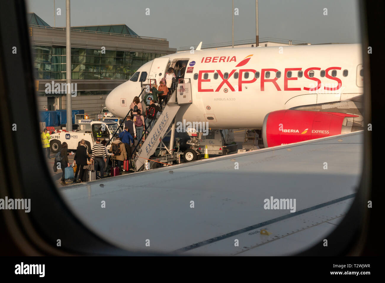 Iberia Express Airbus A320 jet plane at Dublin Airport and passengers people boarding commercial flight as seen through an airplane window Stock Photo