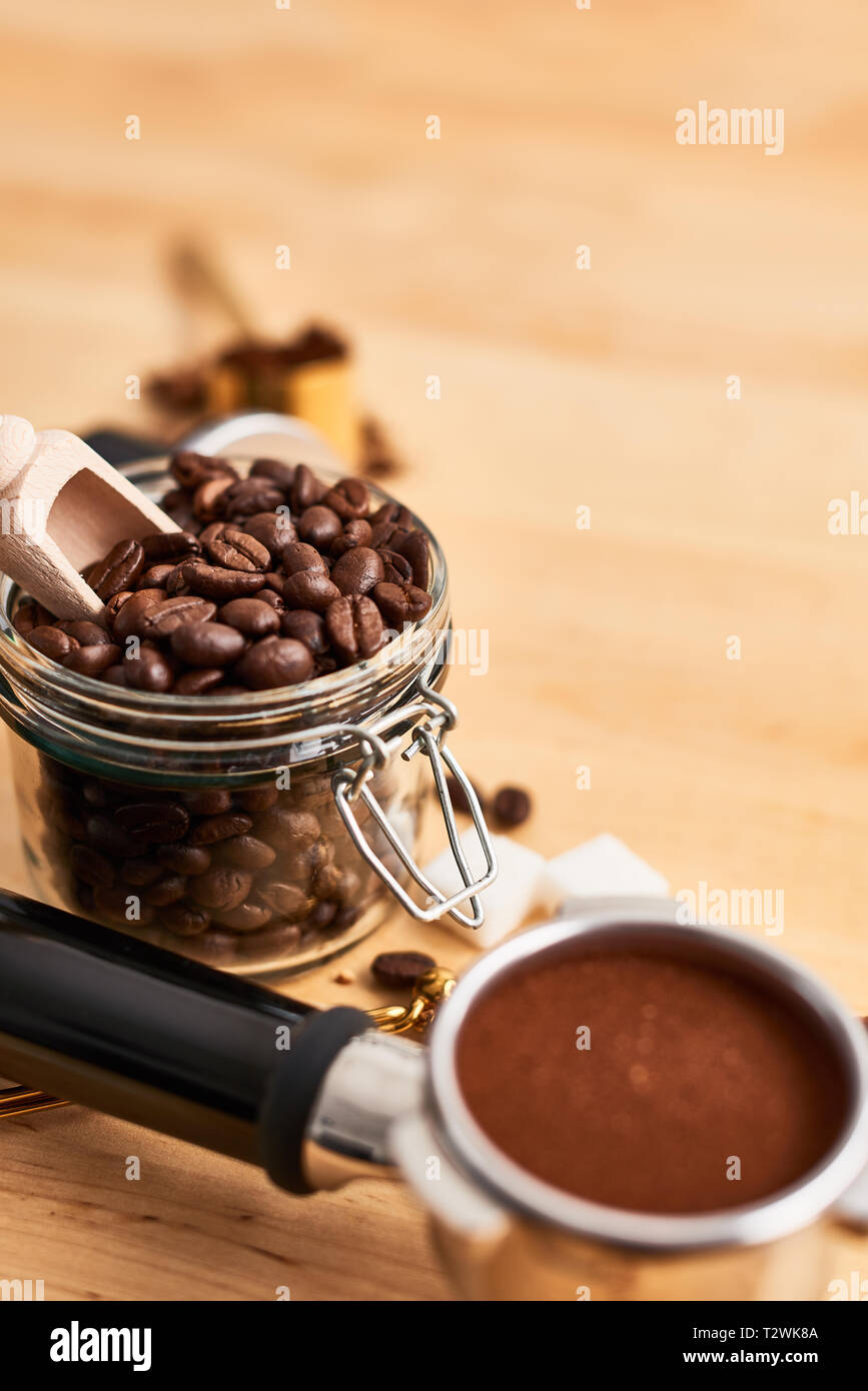 Freshly roasted coffee beans in a glass jar, portafilter and tamper on wooden background. Coffee background. Copy space for text. Barista concept. Stock Photo