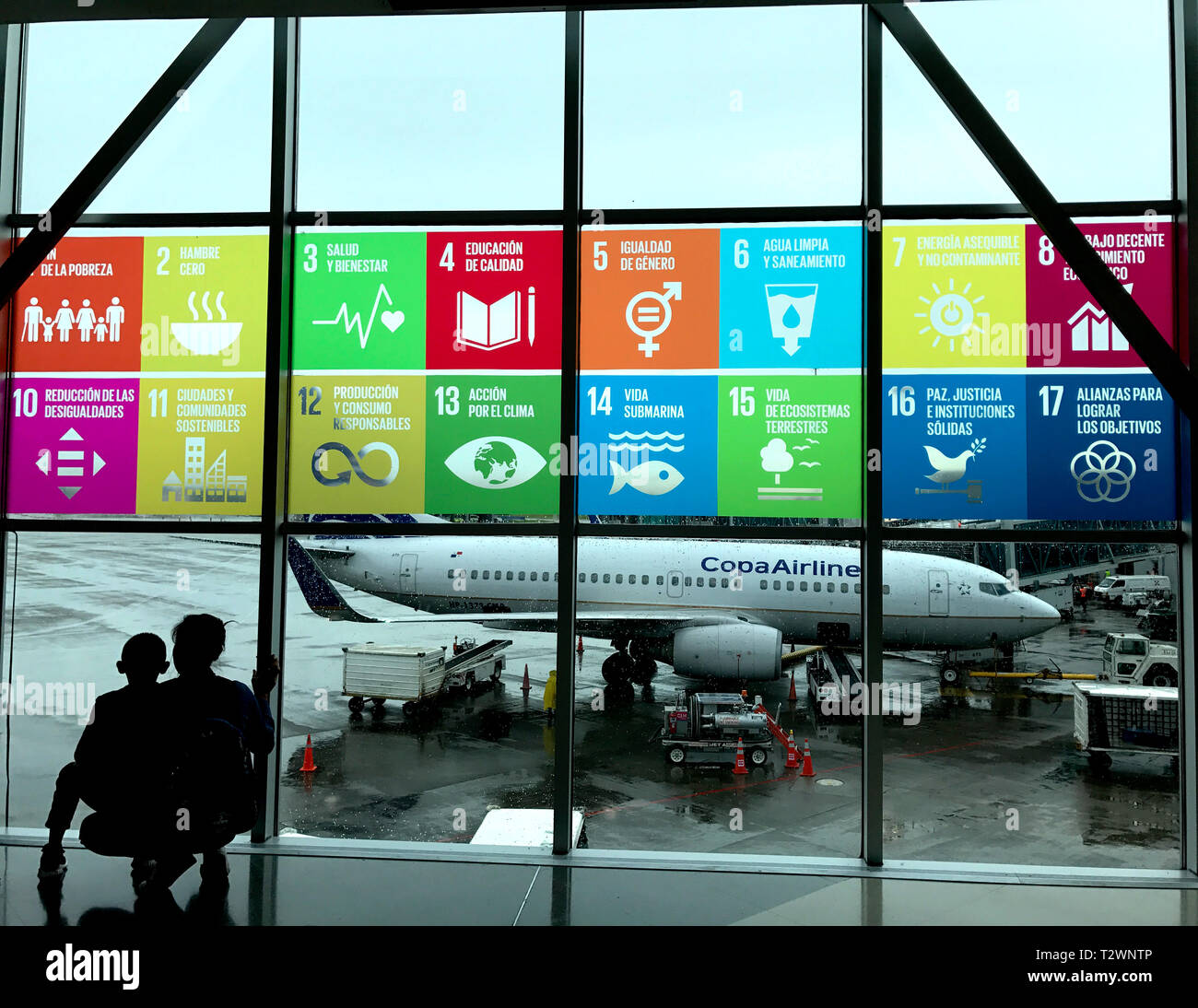 The Global Goals displayed in Spanish on the windows at Panama City Tocumen International Airport. Mother and child looking out to see the planes. Stock Photo