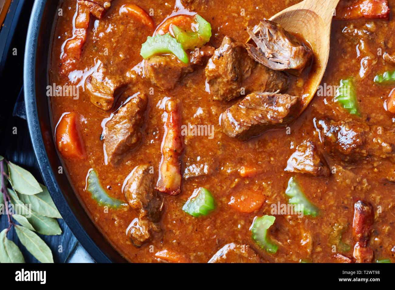 overhead view of traditional irish beef and beer stew with carrots, celery stalk, carrots and spices in a dutch oven on a black wooden table, view fro Stock Photo