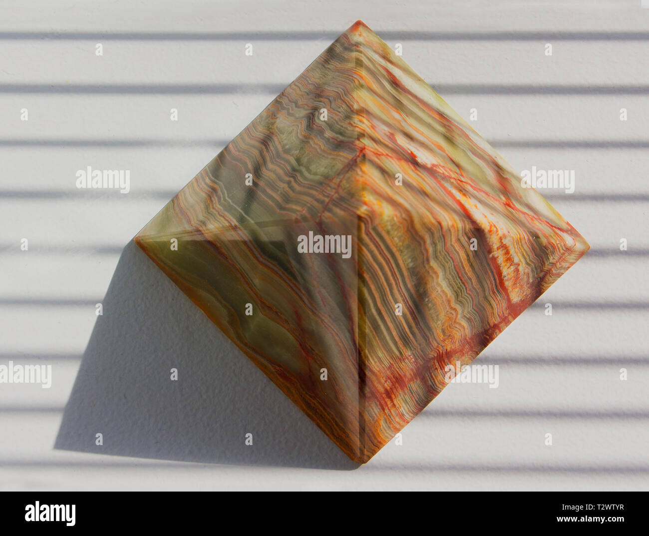 Decorative pyramid sits on a window sill. Shadows cast by pyramid and window blinds. Stock Photo
