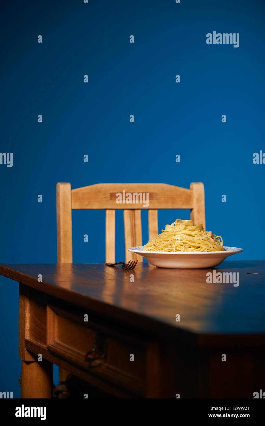 Eine Portion Spaghetti steht auf einenem Holztisch vor einer petrol farbenen Wand Stock Photo