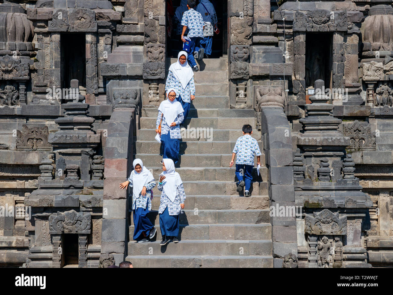 Young school girls walking down the stairs at the Vishnu shrines of the Prambanan temple complex on a sunny day. Java, Indonesia. Stock Photo