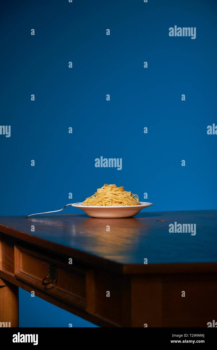 Eine Portion Spaghetti steht auf einenem Holztisch vor einer petrol farbenen Wand Stock Photo