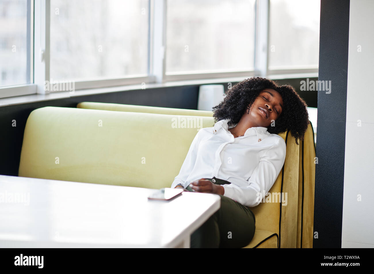 Tired after work. Сheerful business african american lady with afro hair,  wear white blouse and green pants posed in cafe, sleep with closed eyes  Stock Photo - Alamy