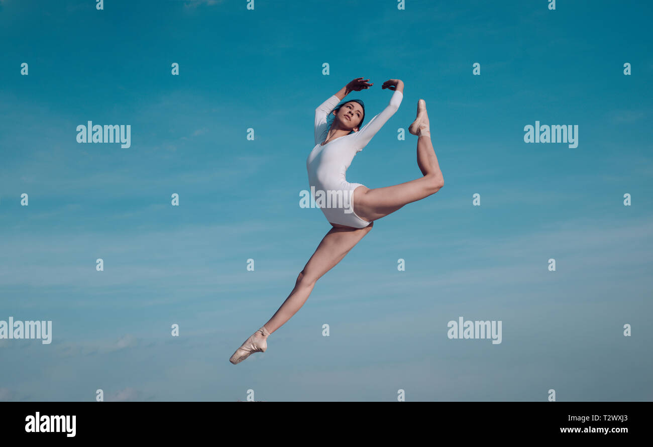 Feels like flying. Young ballerina jumping on blue sky. Pretty girl in dance wear. Cute ballet dancer. Concert performance dance. Practicing art of cl Stock Photo