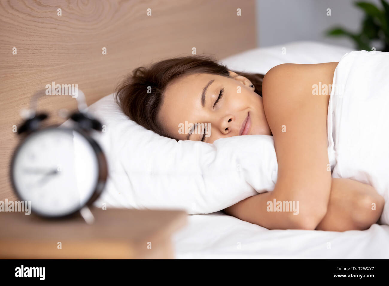 Pretty female sleeping on bed alarm clock on bedside table Stock Photo