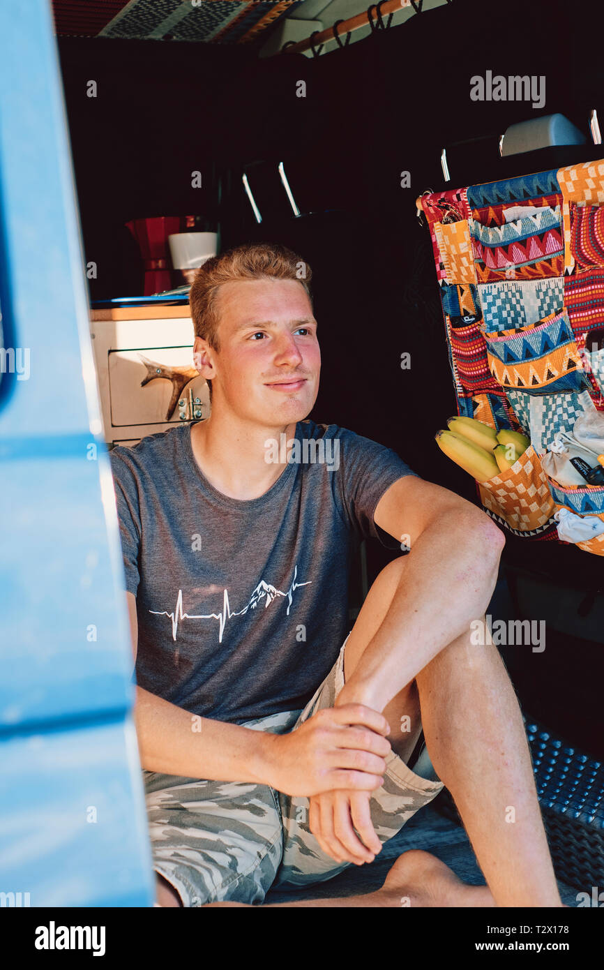 A location lifestyle portrait of a young millennial van life instagrammer living and traveling in his self build camper van / van homes / vanlife / Stock Photo