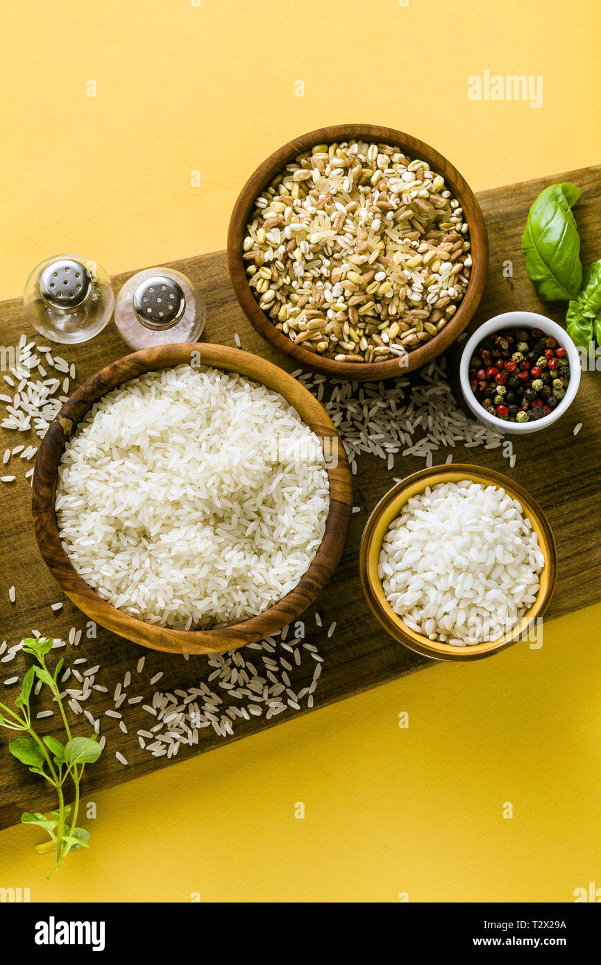 Different types of rice on a wooden board made from olive wood. Food background with basil