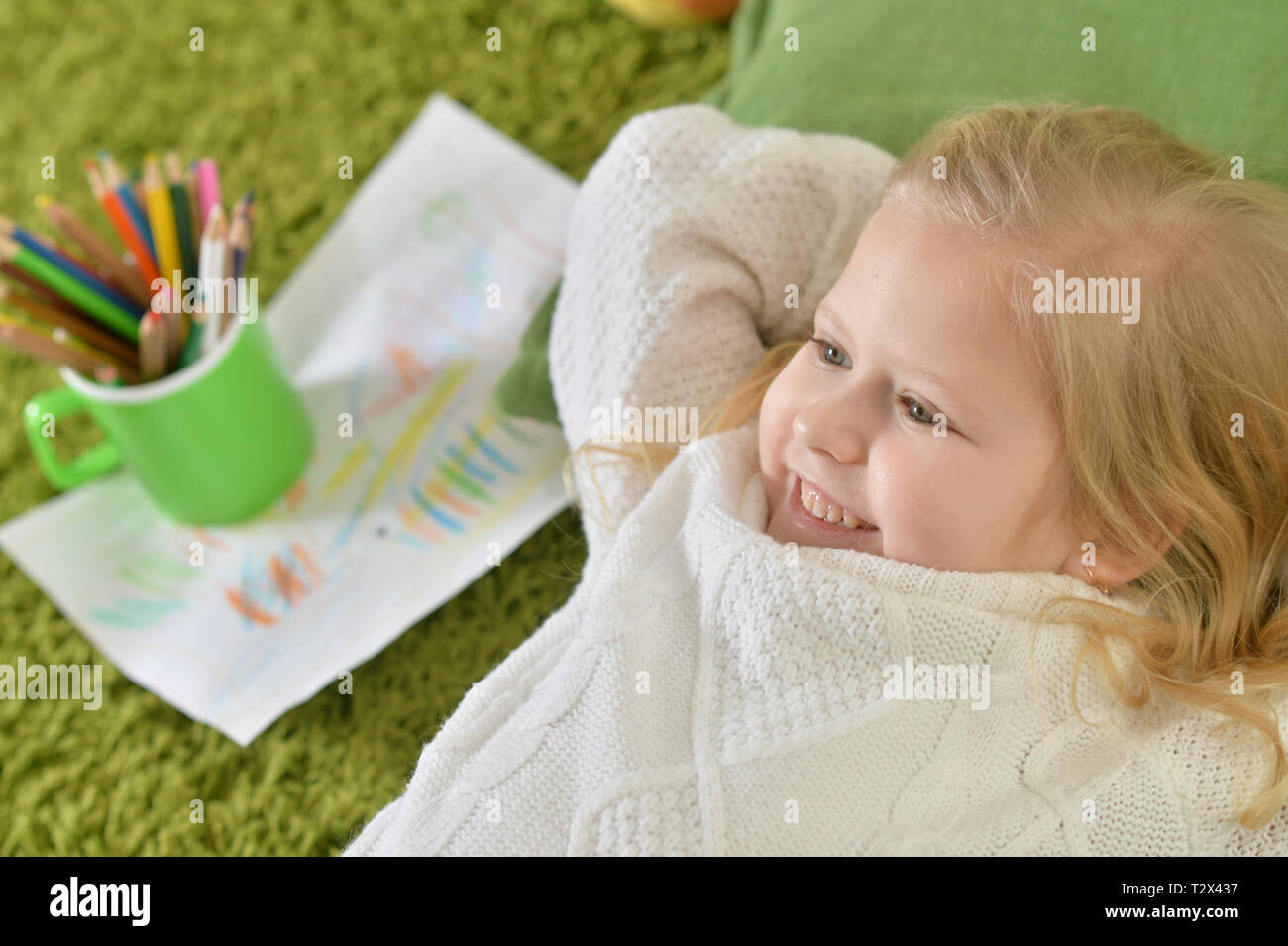 Cute little girl lying on green carpet at home Stock Photo - Alamy