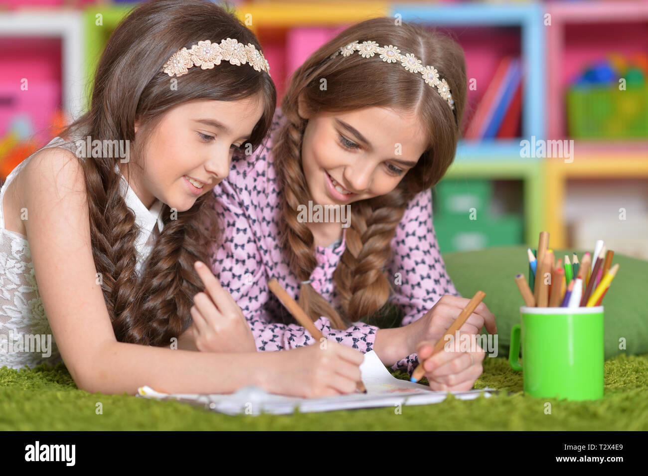 Two cute little girls drawing with pencils while lying on floor Stock ...