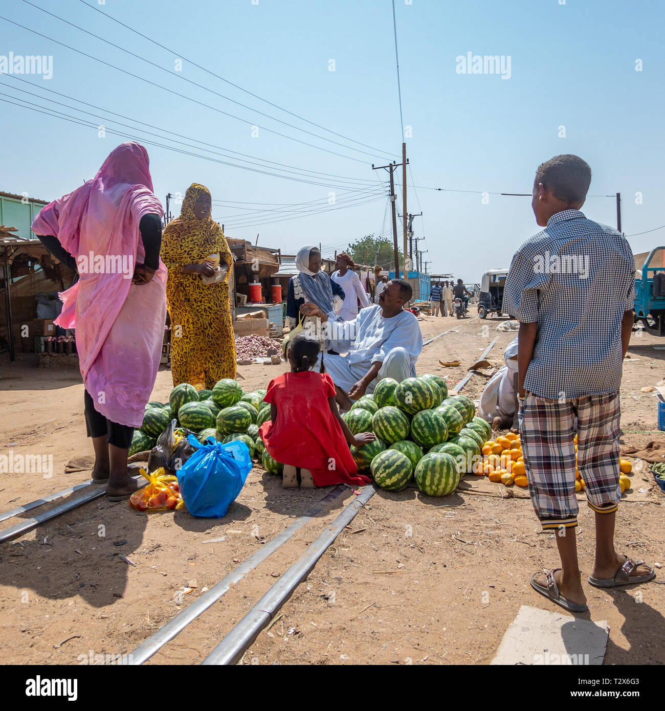 Nuri, Sudan, February 9., 2019: Market stall in Sudan with watermelons, with a woman in a blue skirt, a woman with trousers, a little young girl with  Stock Photo