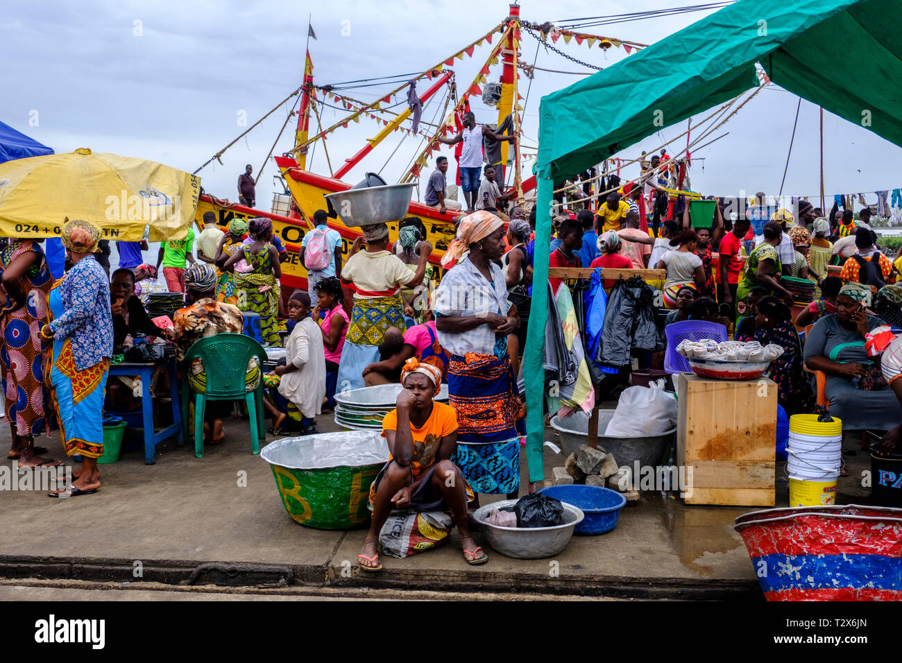 SEKONDI TAKORADI, GHANA – 10 APRIL 2018: Tired and weary looking woman sits in front of busy vibrant scene full of color at Bosomtwi Sam Fishing Harbo Stock Photo