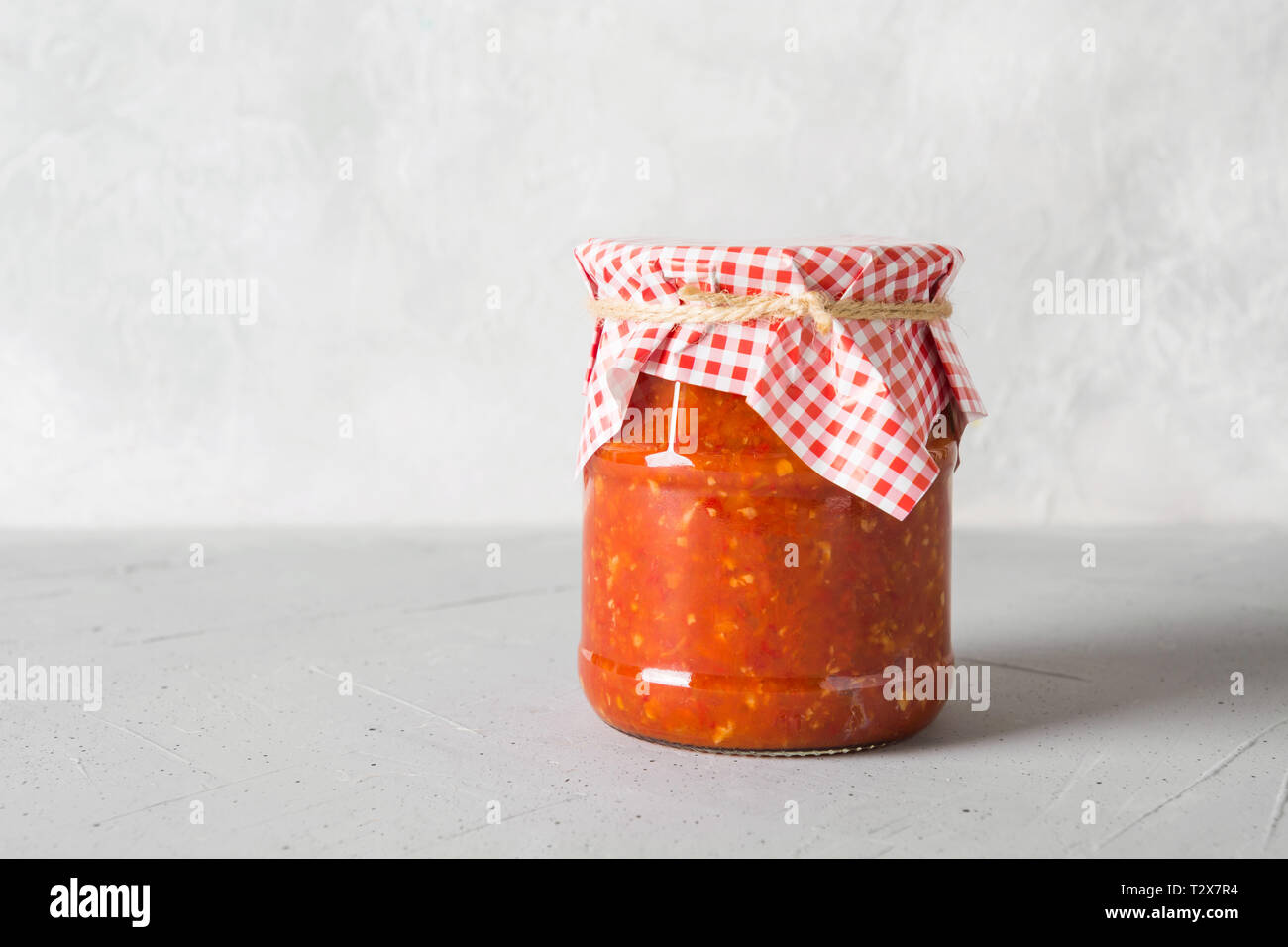Vegetable sauce adjika with tomatoes, garlic, bell peppers in jar on light background. Space for text. Stock Photo