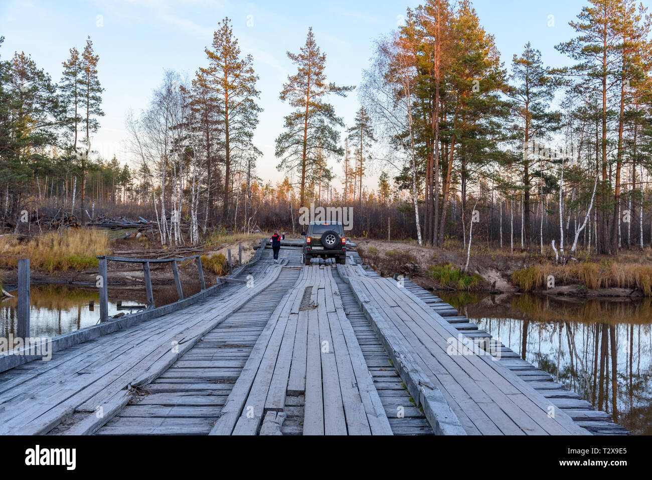 SUV moves on a wooden bridge over a river in the forest Stock Photo