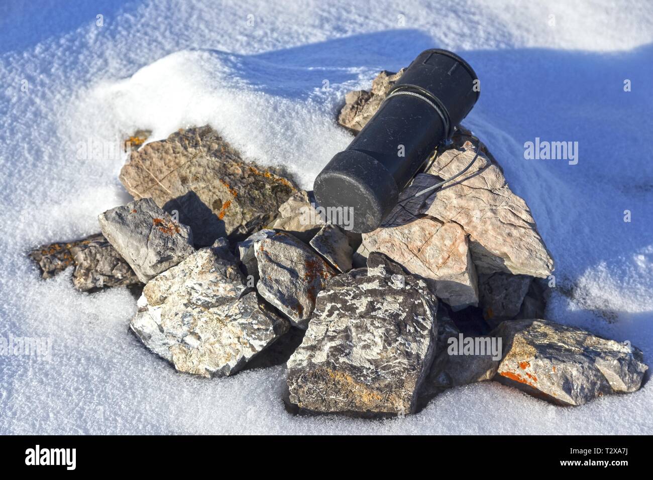 Weathered Black Metal Cylinder Steel Cable. Traditional Climber Register Cairn Rock Pile. Rocky Mountain Peak Summit Snow Canadian Rockies Stock Photo