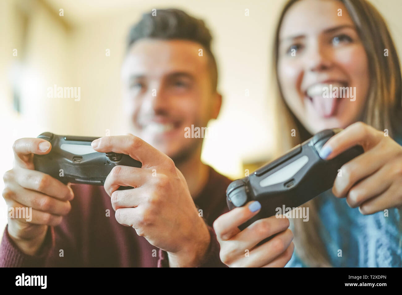 Happy friends playing video games in their apartment - Hilarious young couple having fun with new trend console technology Stock Photo