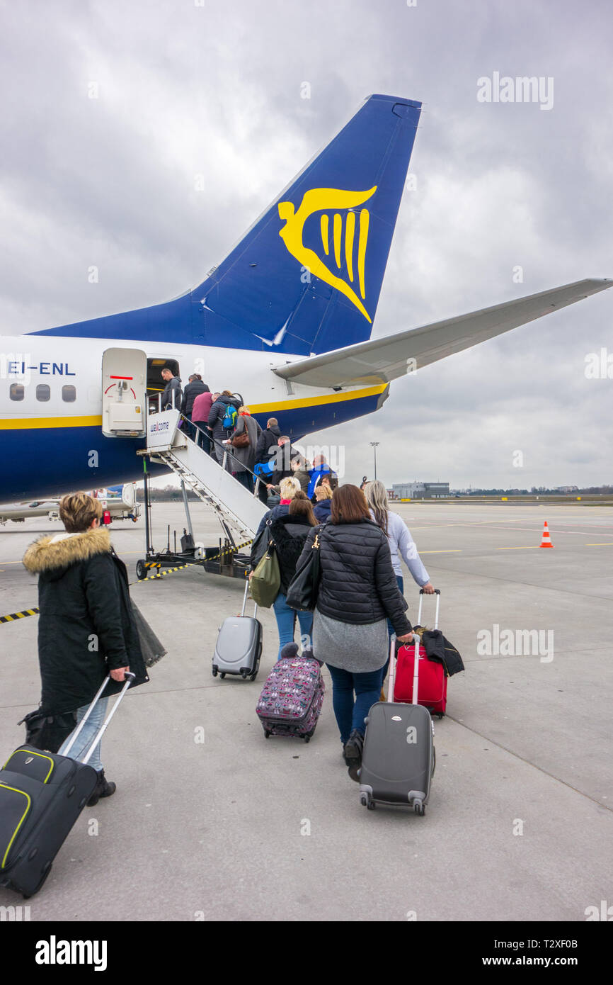 Passengers boarding for a flight on a Ryanair plane pulling along wheeled baggage as hand luggage to go in overhead lockers Stock Photo