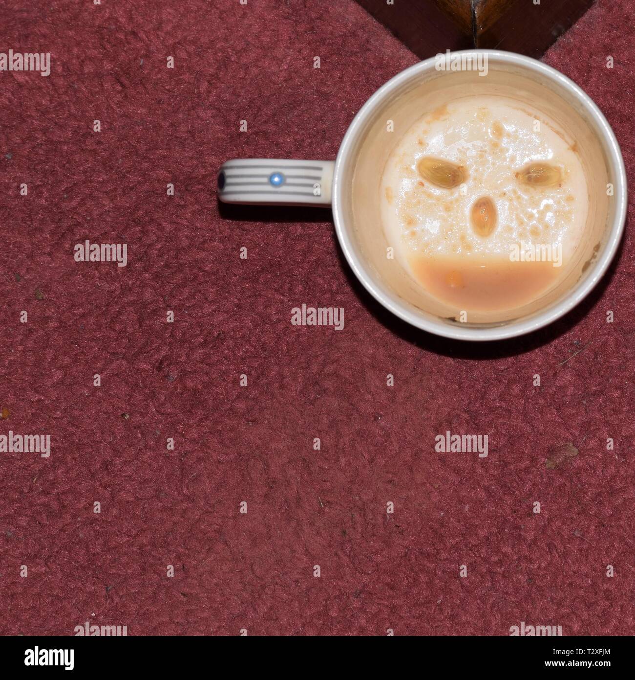 A white cup, on a carpet, with a smiley face designed with lemon pip eyes and coffee dregs mouth. Fun to amuse children and folk in a festive mood. Stock Photo
