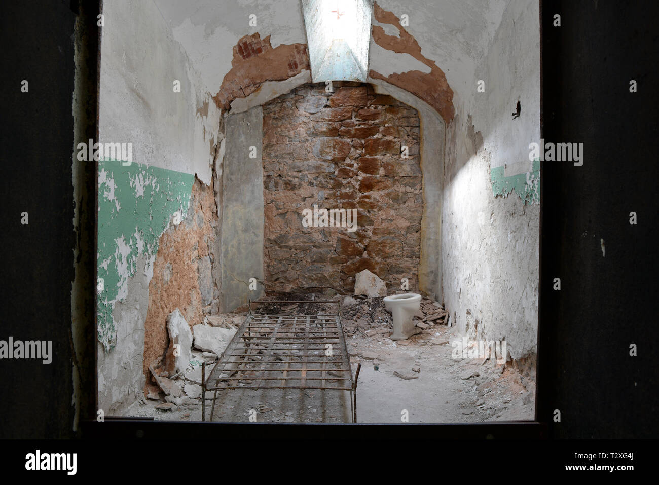 Empty Jail Cell With Bed Frame and Skylight In an Abandoned Prison - Eastern State Penitentiary Stock Photo