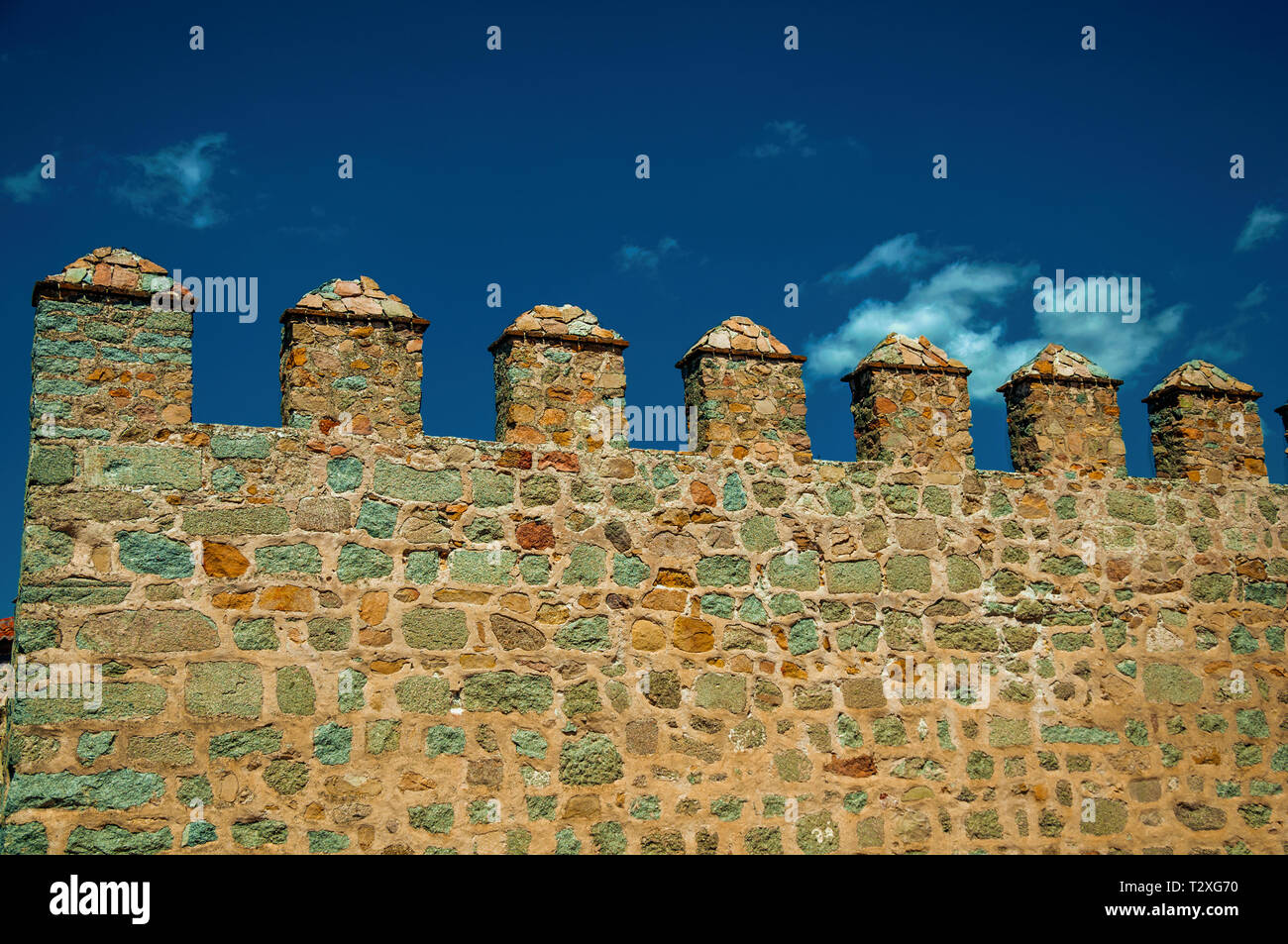 Battlement with merlons and crenels over rough stone wall encircling the town of Avila. With an imposing wall around the gothic city center in Spain. Stock Photo