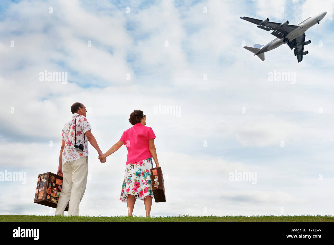 Modern senior caucasian tourists holding hands watching passenger plane Stock Photo