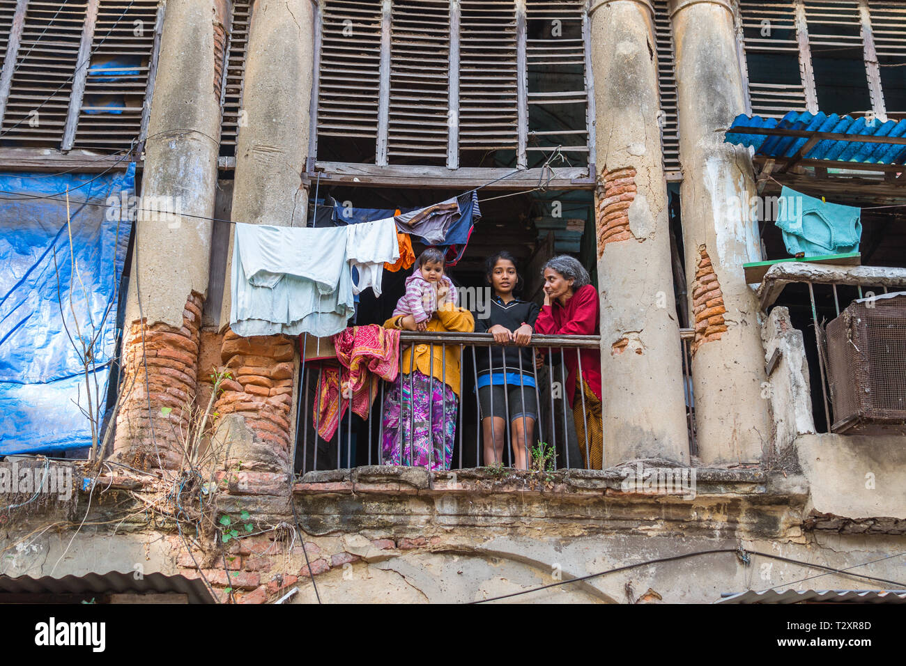 Kolkata, India - January 10, 2015: two women, a girl, and a baby stand on the balcony of an old shabby house with crumbling columns. Stock Photo