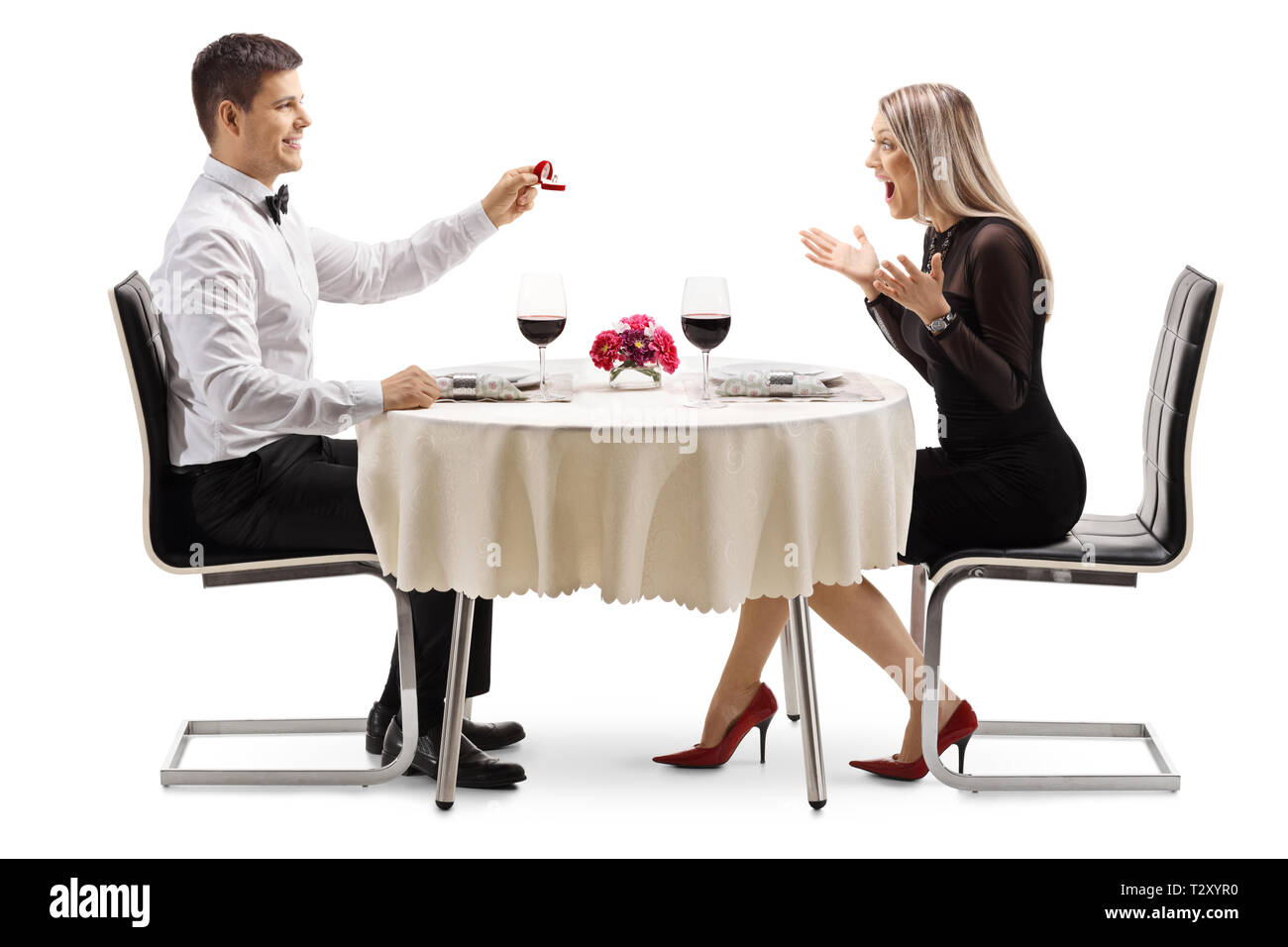 Full length profile shot of a young man proposing a marriage with a ring to a young woman at a restaurant table isolated on white background Stock Photo