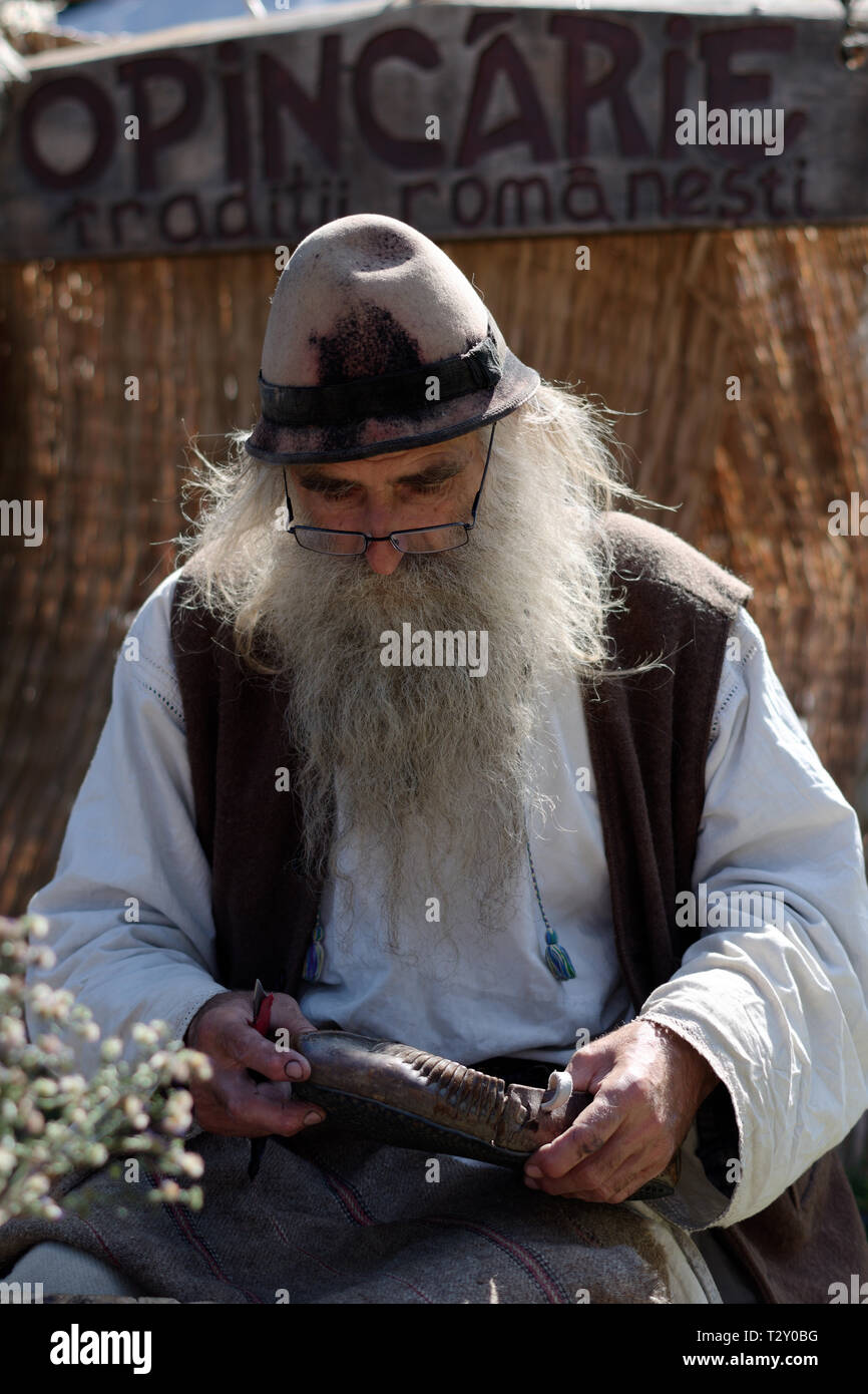 Old Artisan Man Working at a Traditional Pair of Sandals in Leather, Wearing an Old Popular Suite, Festival of Traditional Arts, Bucharest Stock Photo
