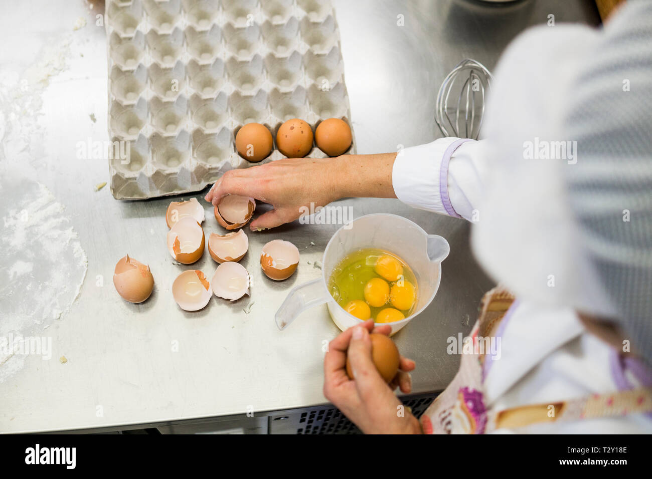woman pastry chef adding eggs to graduated container while making cakes Stock Photo