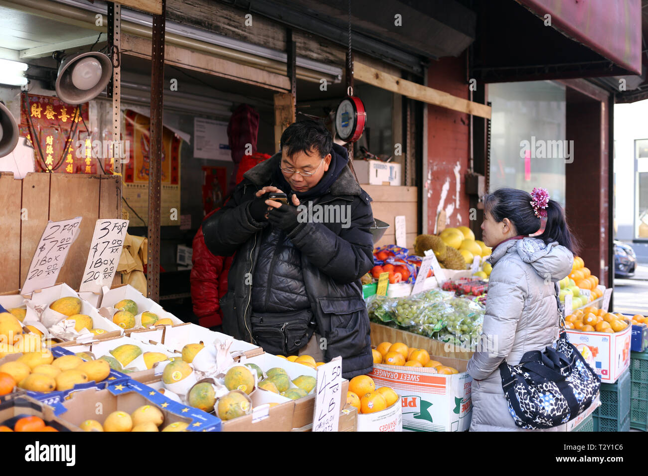 Two unidentified people selling and buying fruits on a store on Chinatown, New York City, NY Stock Photo