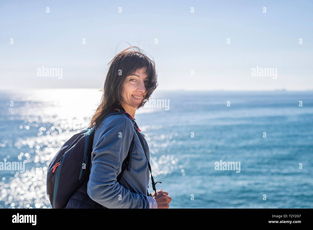 Beautiful woman standing against the sea looking camera and smiling Stock Photo