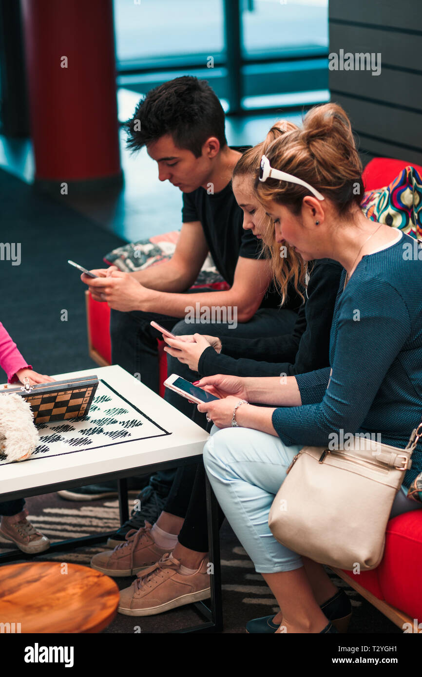 Family members using mobile phones together, sitting on sofa in lounge