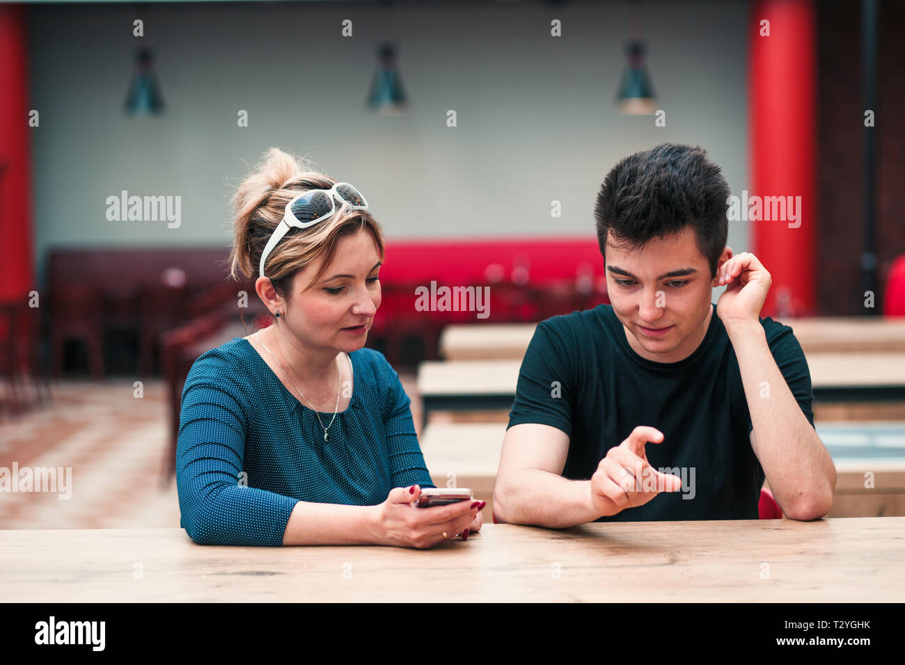 Woman and young man talking together and using mobile phones sitting by a table in cafe Stock Photo