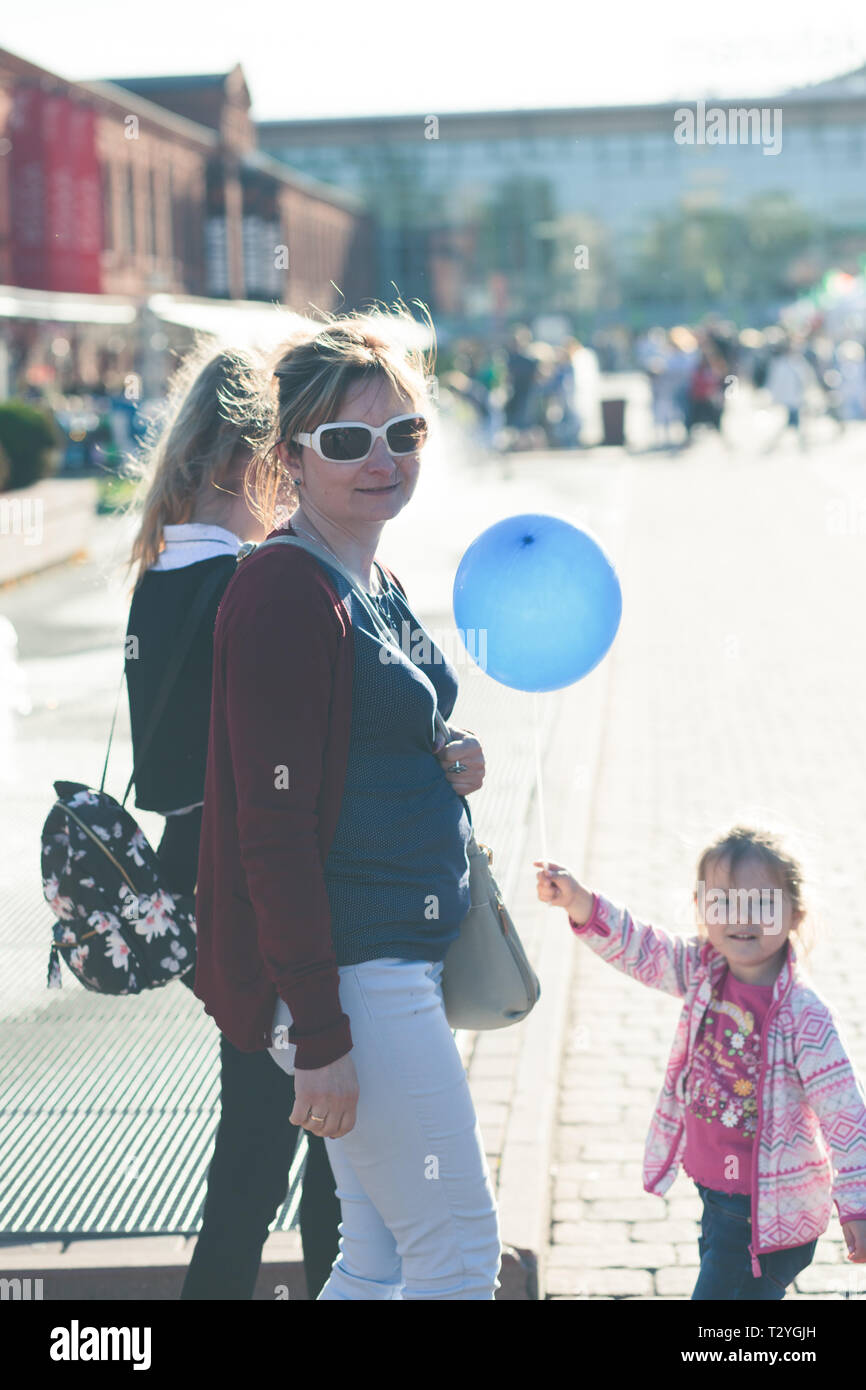 Mother walking with her daughters, spending time in center of city outdoors. Little girl holding blue balloon Stock Photo