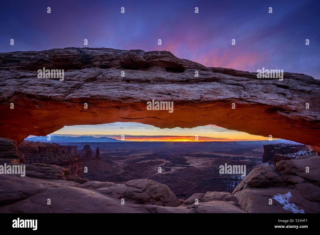 View through arch Mesa Arch at sunrise, Colorado River Canyon with the La Sal Mountains behind, view at Grand View Point Trail, Island in the Sky Stock Photo