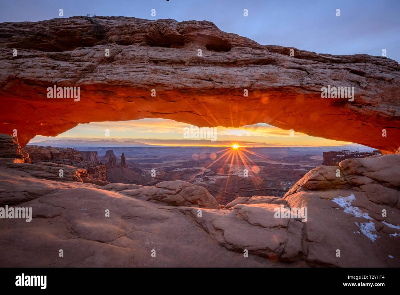 View through arch Mesa Arch at sunrise with sunstar, Colorado River Canyon with the La Sal Mountains behind, view at Grand View Point Trail, Island Stock Photo