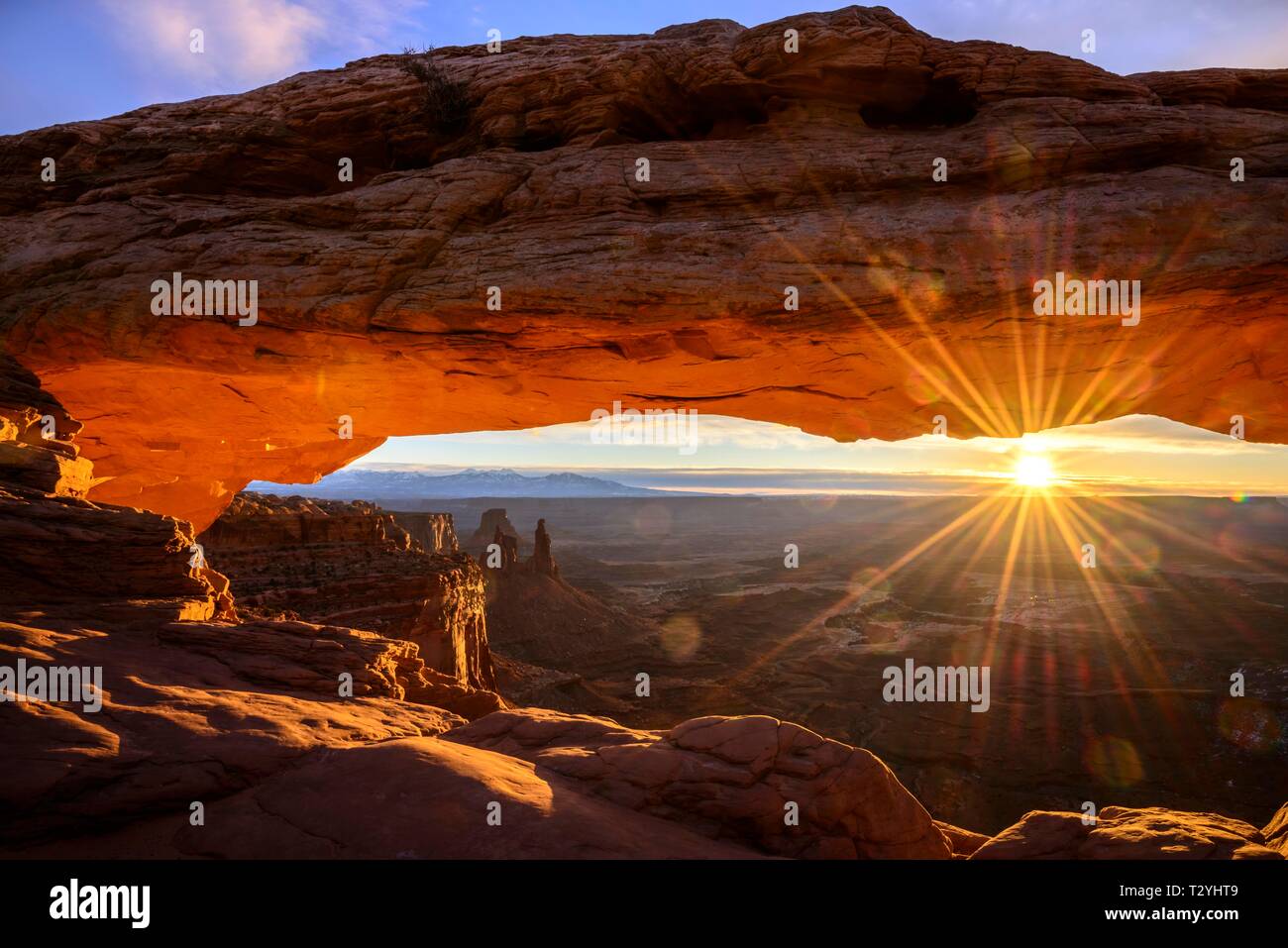 View through arch Mesa Arch at sunrise with sunstar, Colorado River Canyon with the La Sal Mountains behind, view at Grand View Point Trail, Island Stock Photo