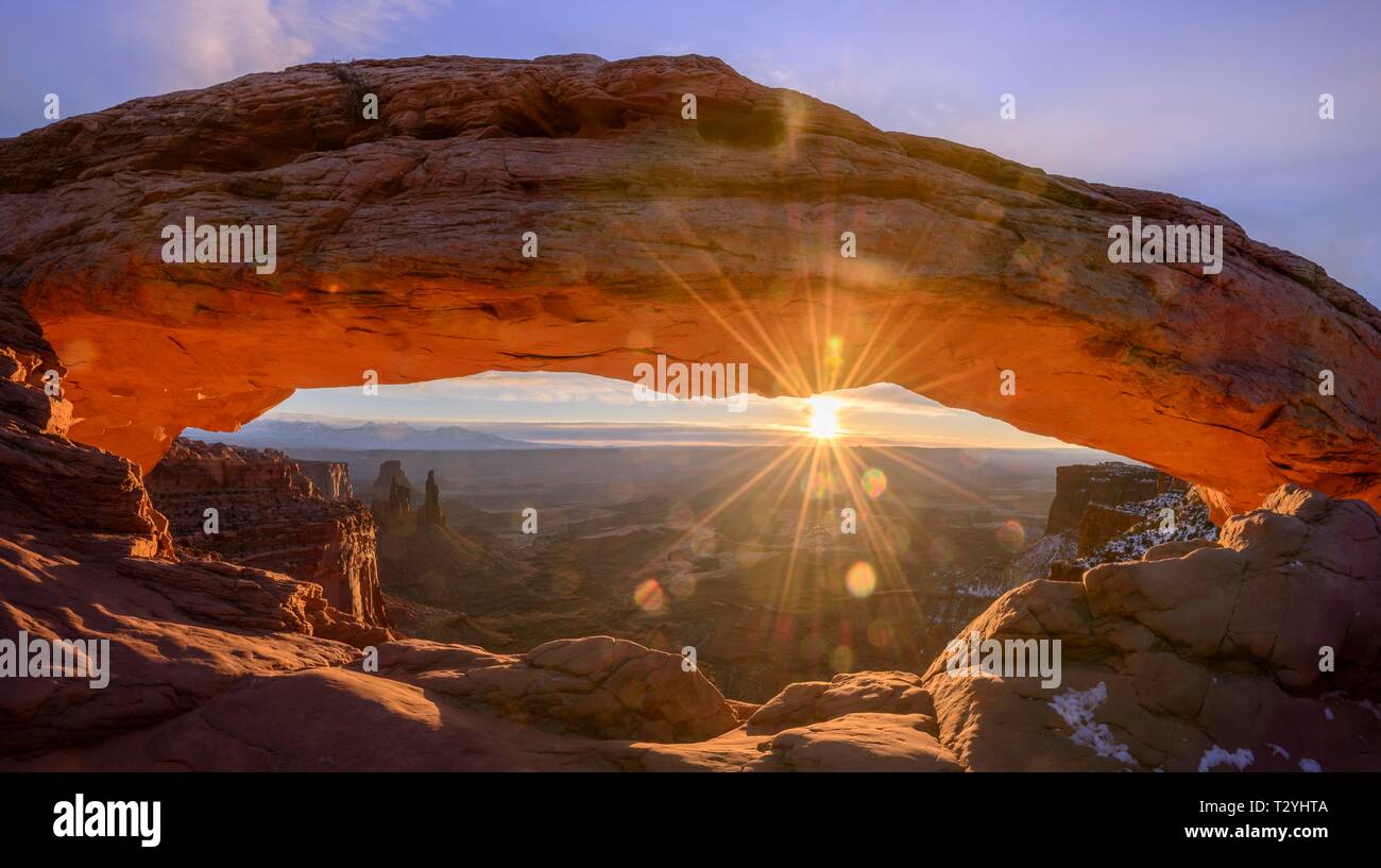 View through arch Mesa Arch at sunrise with sunstar, Colorado River Canyon with the La Sal Mountains behind, view at Grand View Point Trail, Island Stock Photo