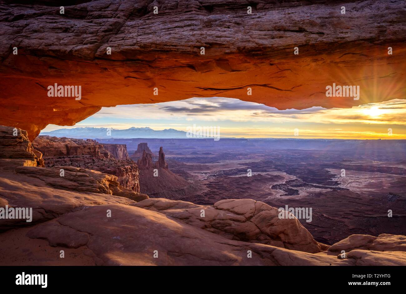View through arch Mesa Arch at sunrise, Colorado River Canyon with the La Sal Mountains behind, view at Grand View Point Trail, Island in the Sky Stock Photo