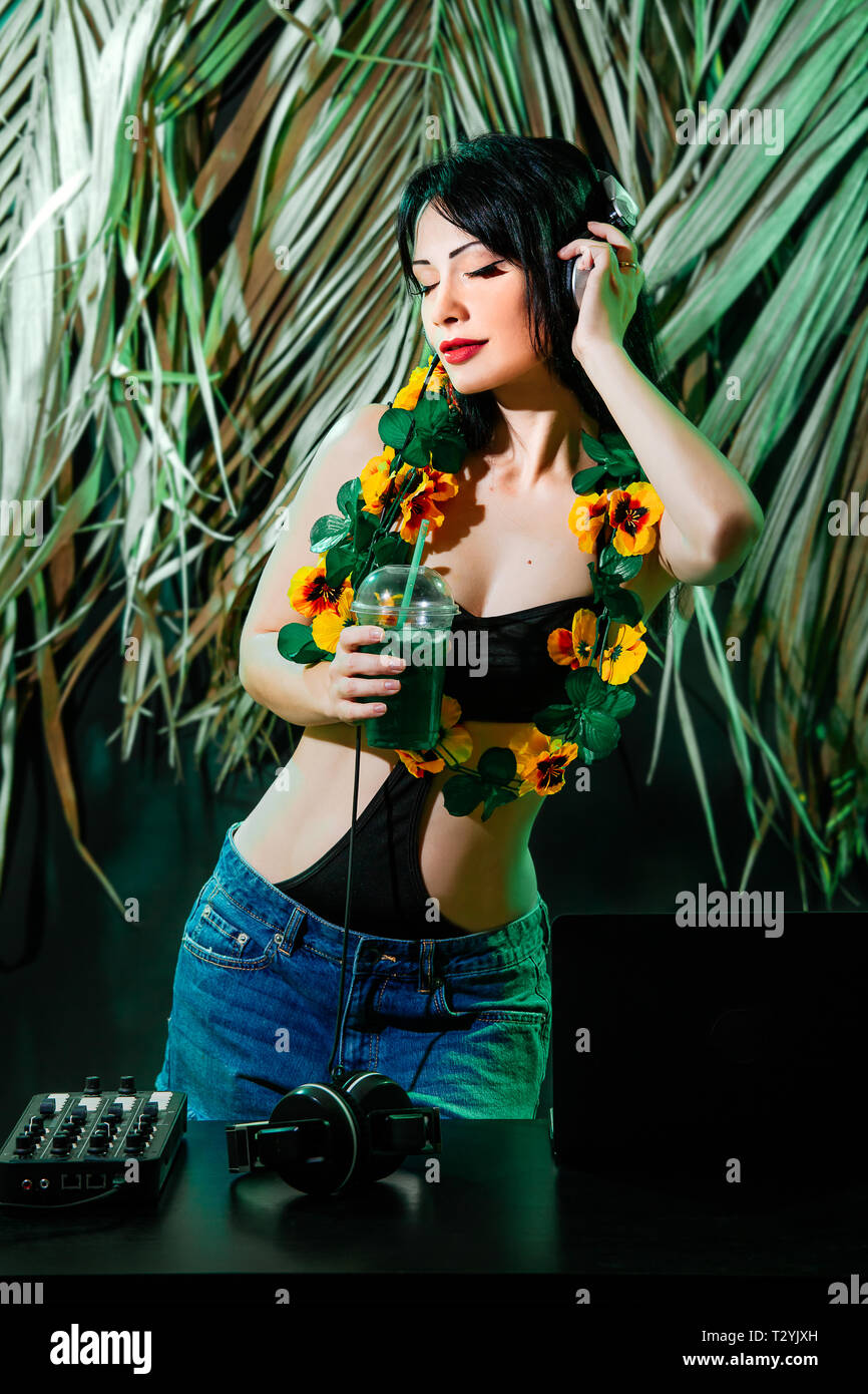 Brunette girl in bikini with cocktail on tropical leaves background. DJ  woman plays music disko party on the equipment in the summer club Stock  Photo - Alamy