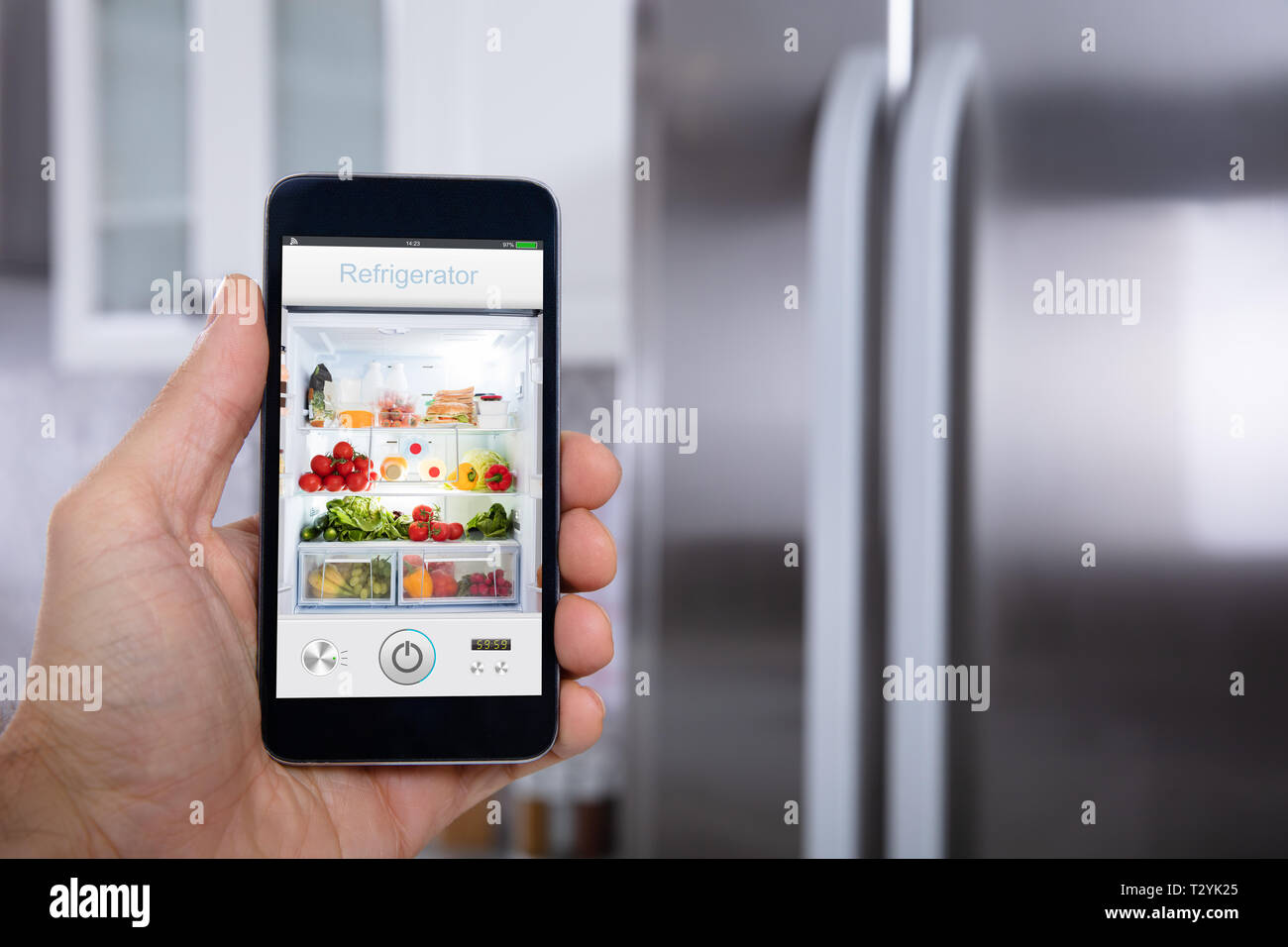 Close-up Of A Person's Hand Operating Refrigerator With Mobile Phone Stock Photo