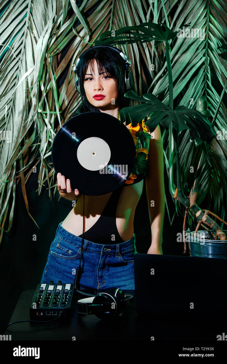 Brunette girl in bikini with vinyl disc on tropical leaves background. DJ  woman plays music disko party on the equipment in the summer club Stock  Photo - Alamy