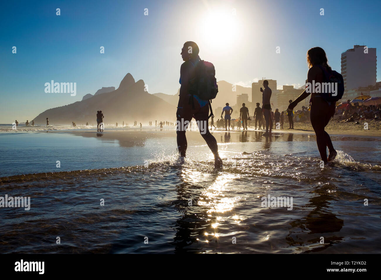 RIO DE JANEIRO - FEBRUARY, 2018: Silhouettes of beachgoers stand in the waves on Ipanema Beach, where scenic sunsets belie a violent crime epidemic. Stock Photo