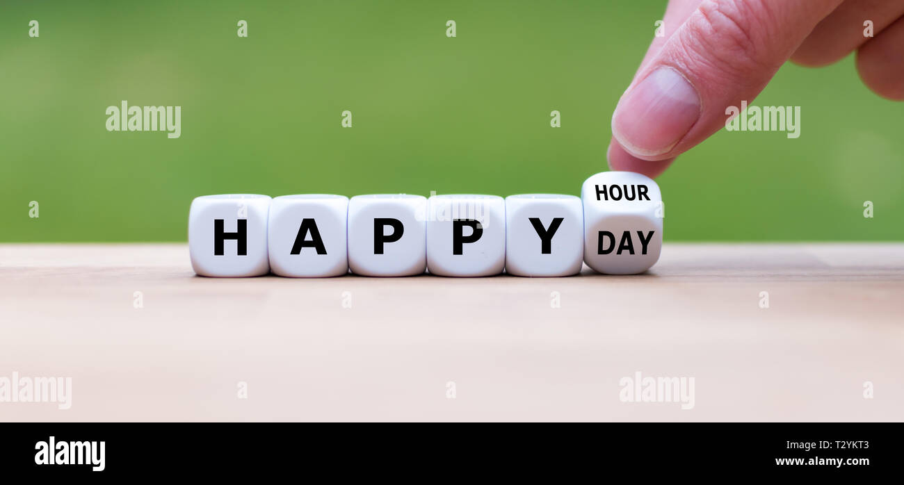 Symbol for a stress-free day. Hand turns a dice and changes the expression 'happy hour' to 'happy day'. Stock Photo