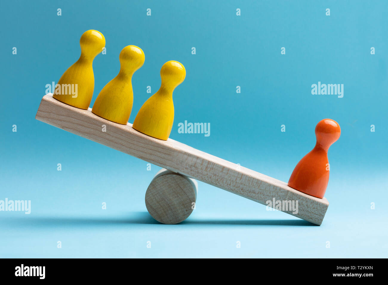Close-up Of Red And Yellow Pawns Figures Balancing On Wooden Seesaw Over Blue Surface Stock Photo
