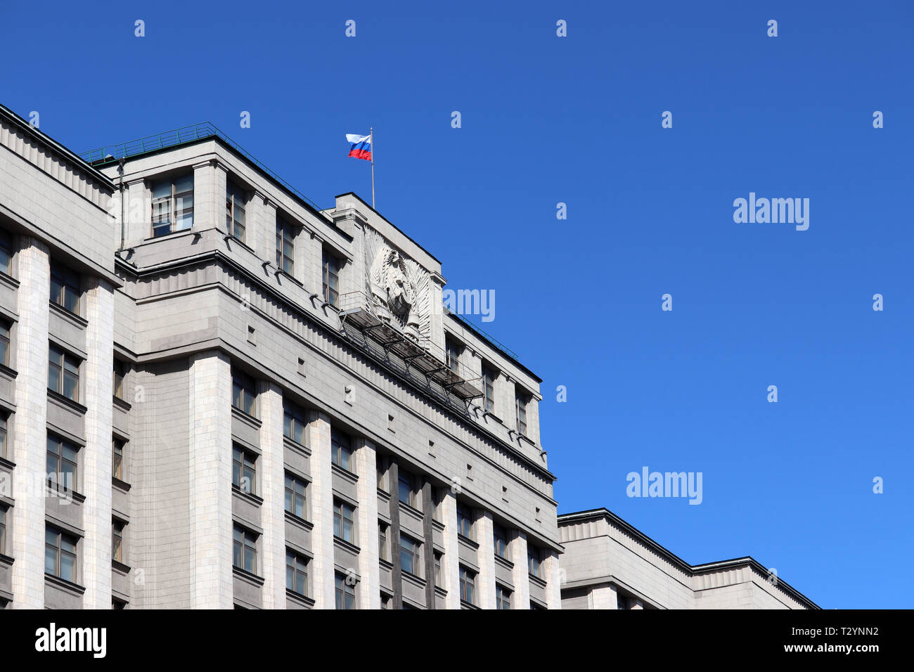 Russian flag on the Parliament building in Moscow against blue sky. Facade of State Duma of Russia with soviet coat of arms, russian authority Stock Photo