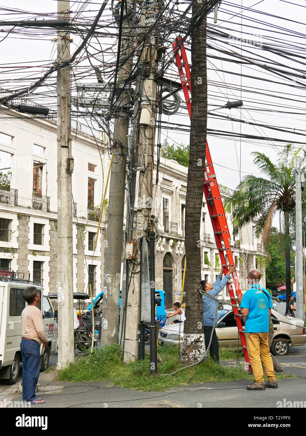 Manila, Philippines: A group of men fixing cables on a post with the help of a ladder in the historical city of Intramuros Stock Photo